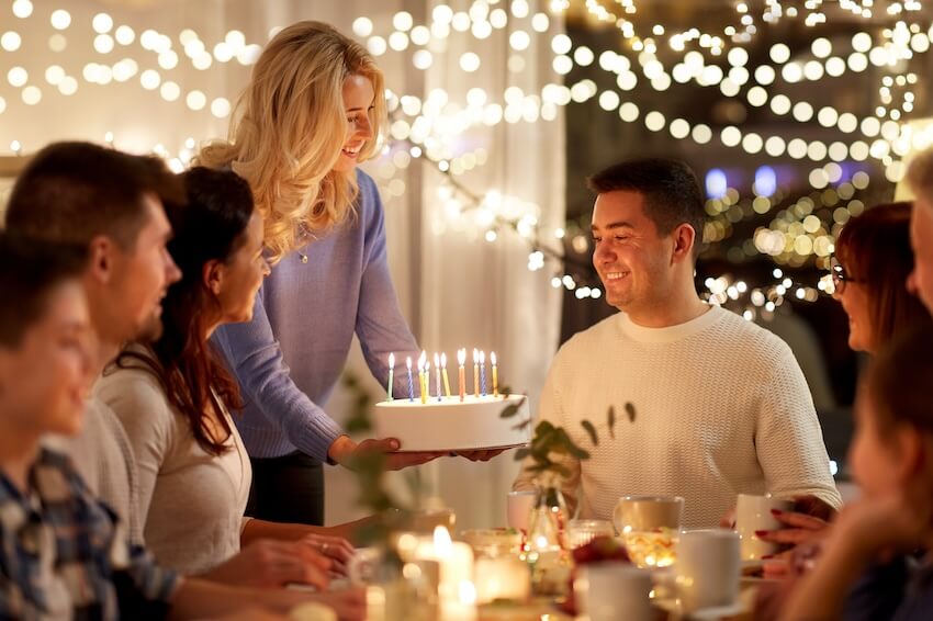 40th birthday party ideas for men: woman handing a birthday cake with lit candles to a celebrant